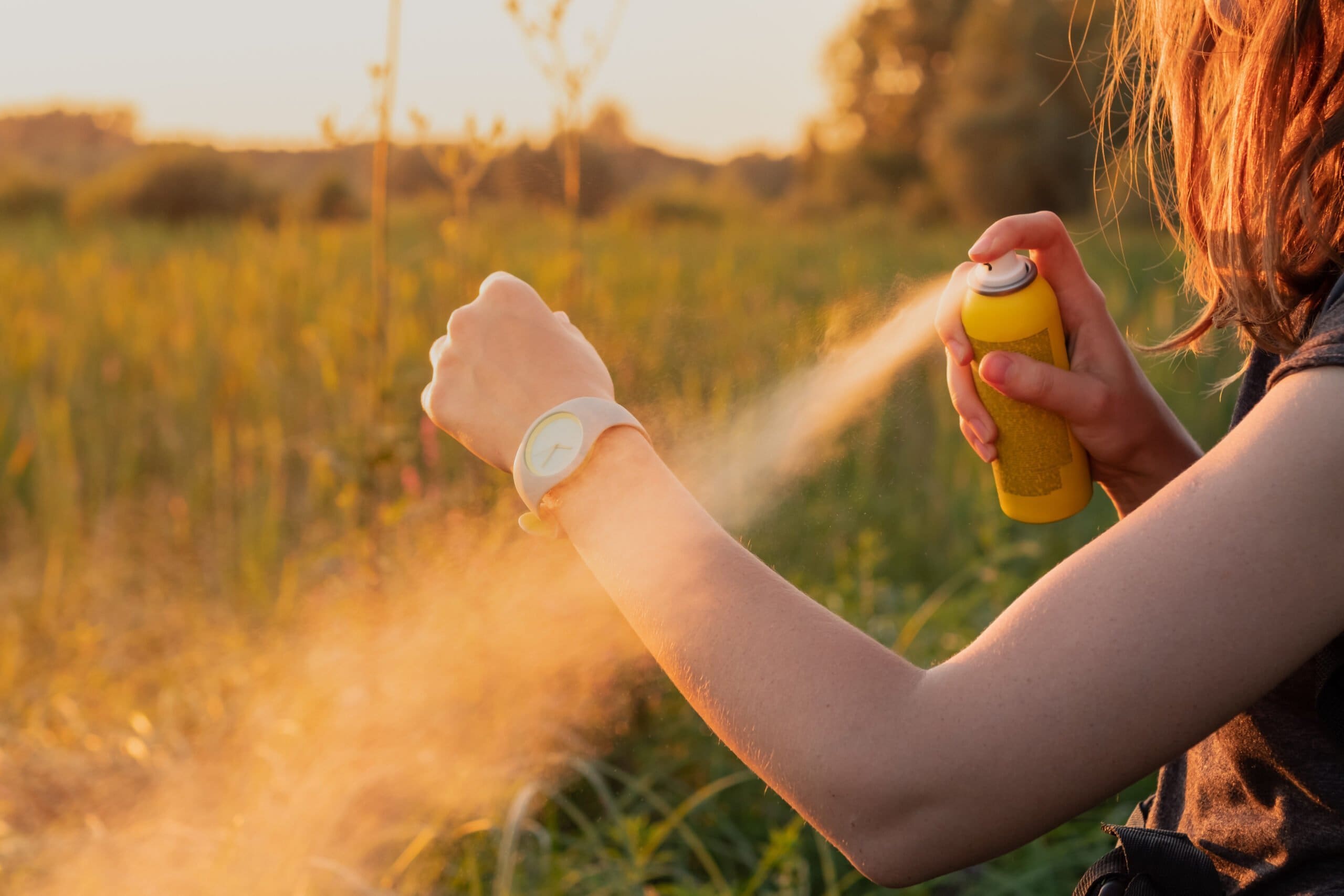 Woman using mosquito spray repellant in a field