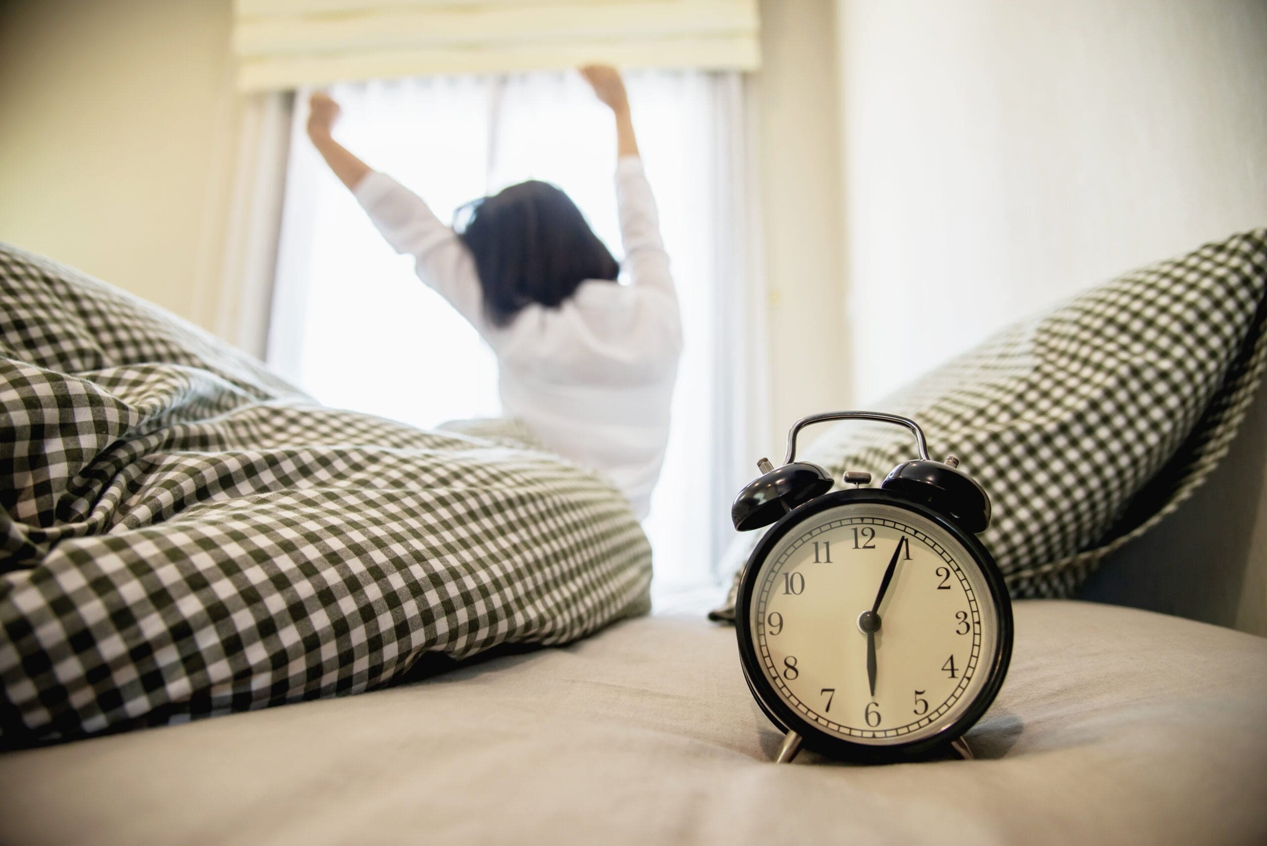 Woman waking up early and stretching in bed with an alarm clock