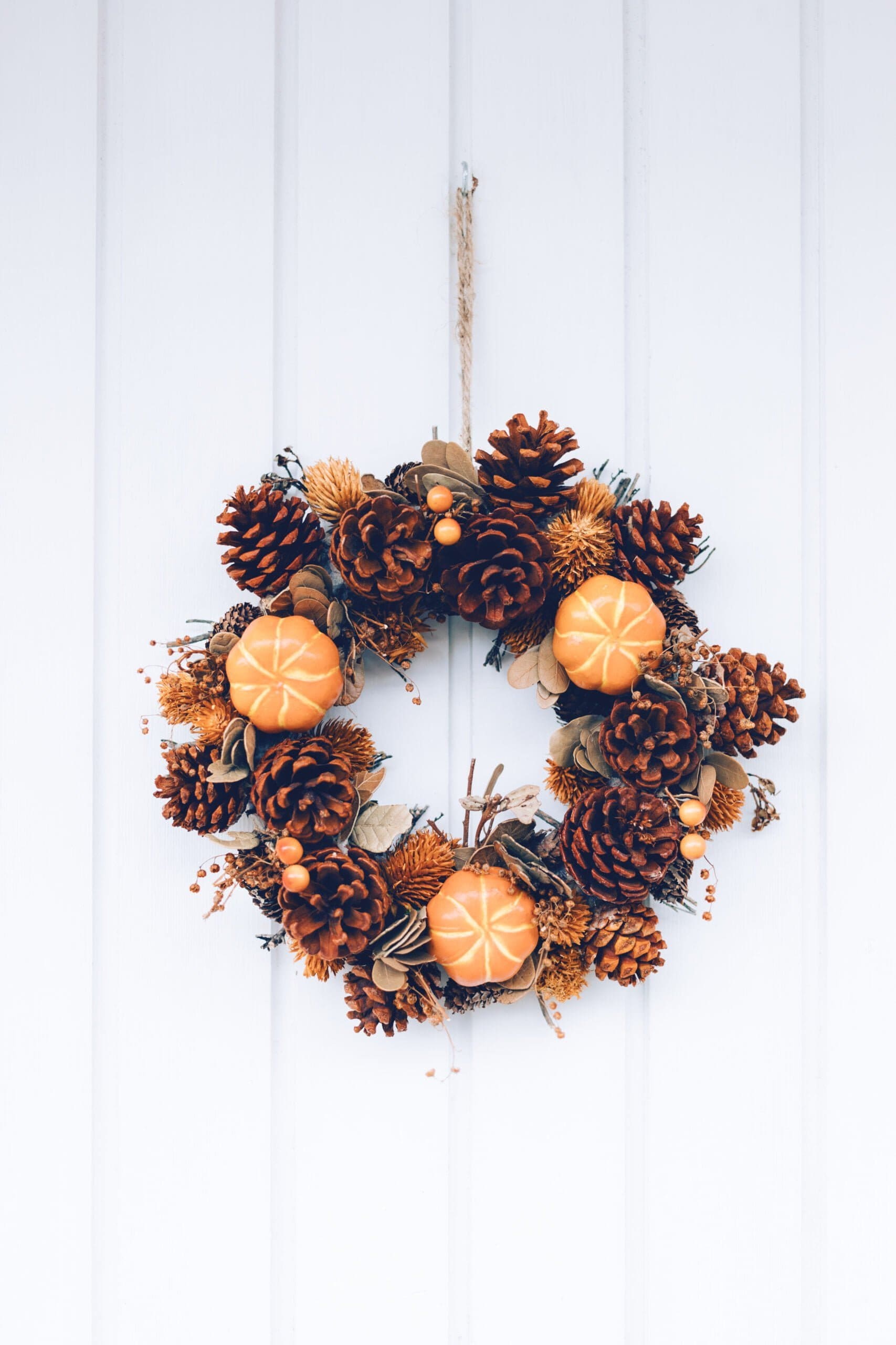 door-wreath-decorated-fall-colors-with-mini-pumpkins-pinecones-white-wooden-door