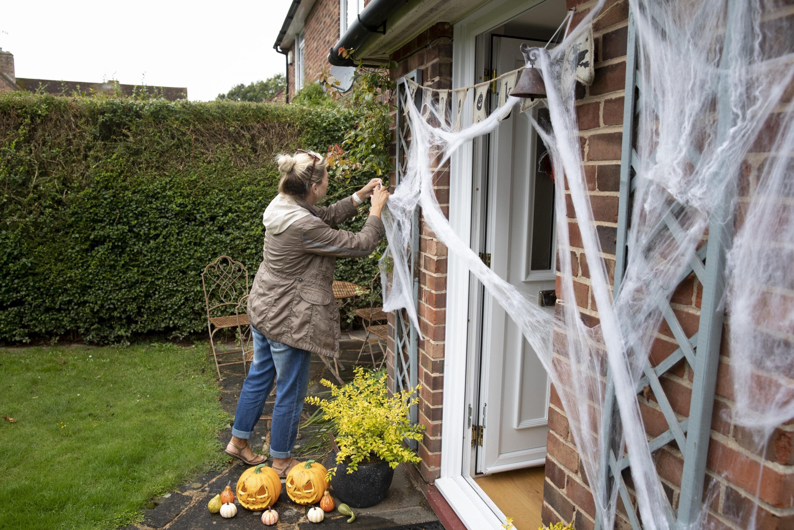 woman putting cobwebs and other halloween decorations on her house for hallowee