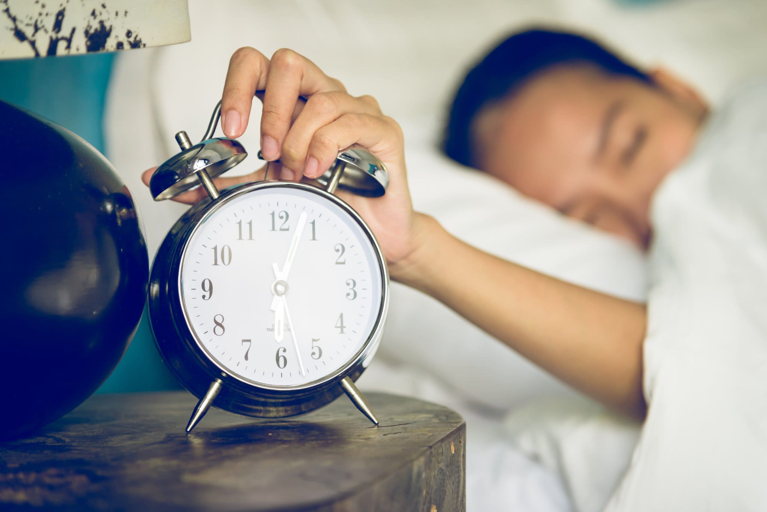 woman pressing alarm clock waking up after change in clocks for daylight savings time
