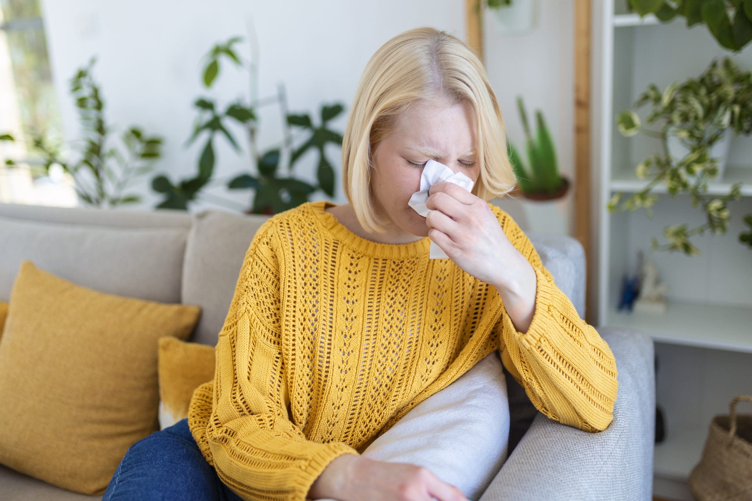 woman sneezing on couch because of allergens in home wanting to build and maintain a hypoallergenic home