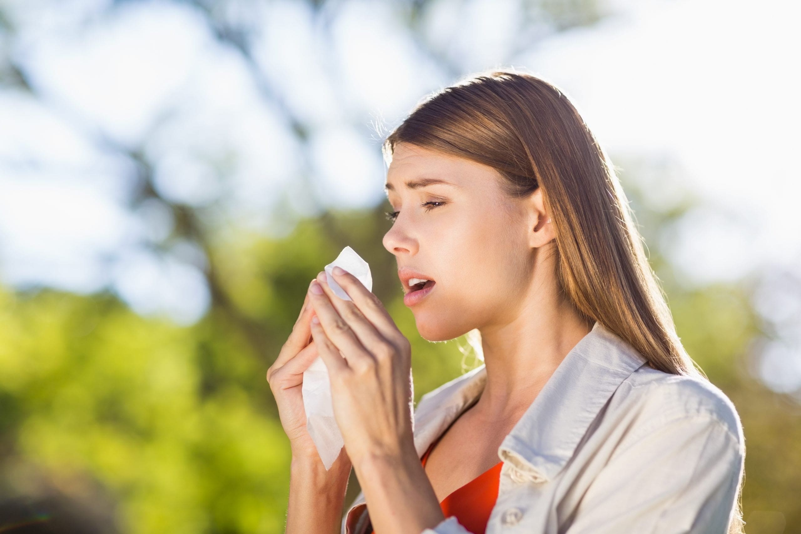 Woman walking outside using tissue to sneeze because of spring allergies